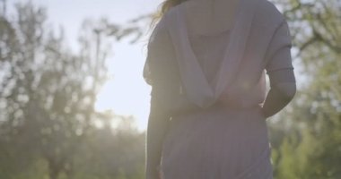 Kamera, havadar pembe elbiseli kızı elma bahçelerinde yeşil çimlerin üzerinde yürürken takip ediyor. Arkadaki ışığa karşı filme alındı..