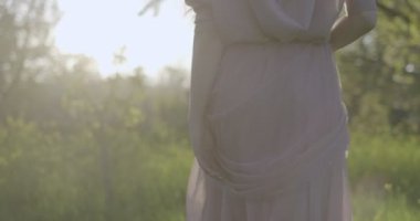 Kamera, havadar pembe elbiseli kızı elma bahçelerinde yeşil çimlerin üzerinde yürürken takip ediyor. Arkadaki ışığa karşı filme alındı..