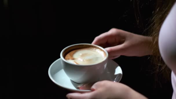 女性手中的黑咖啡和茶托的特写 杯子和茶托是白色的 穿着浅粉色短裙的女人 在黑色房间拍摄 — 图库视频影像