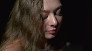 Uzun açık kahverengi saçlı, gri gözlü, beyaz bardaktan zevk alarak kahve içen bir kızın yakın çekimi. Siyah bir arkaplanda tam yüz olarak çekilen