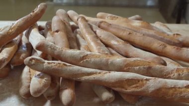 Fresh baked long baguette breads lie on the wooden table sprinkled with flour in a pile. Slow motion
