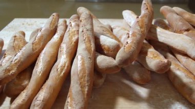 Fresh baked long baguette breads lie on the wooden table sprinkled with flour in a pile. Slow motion