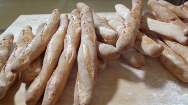 Fresh baked long baguette breads lie on the wooden table sprinkled with flour in a pile. Slow motion