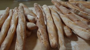 Fresh baked long baguette breads lie on the wooden table sprinkled with flour in a pile. Slow motion
