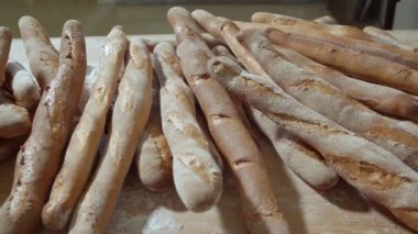 Fresh baked long baguette breads lie on the wooden table sprinkled with flour in a pile. Slow motion