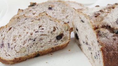 Close-up of sliced pieces and half of rye raisin bread on the white table. Also we see black handle kitchen knife and white milk jug and yellow cup on the back