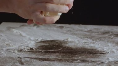 Male hands divide baking dough into three equal shares on a wooden board sprinkled with flour. Filmed on black background