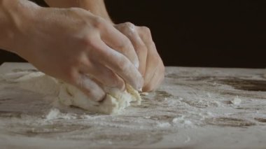 Male hands divide baking dough into three equal shares on a wooden board sprinkled with flour. Filmed on black background