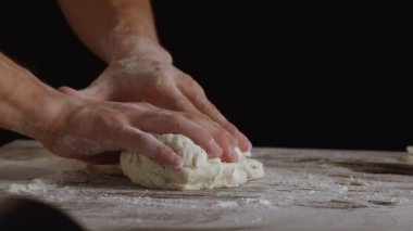 Male hands divide baking dough into three equal shares on a wooden board sprinkled with flour. Filmed on black background