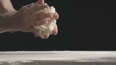 Male hands divide baking dough into three equal shares on a wooden board sprinkled with flour. Filmed on black background