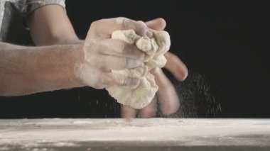 Male hands divide baking dough into three equal shares on a wooden board sprinkled with flour. Filmed on black background