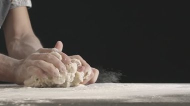 Male hands divide baking dough into three equal shares on a wooden board sprinkled with flour. Filmed on black background