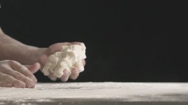 Male hands divide baking dough into three equal shares on a wooden board sprinkled with flour. Filmed on black background