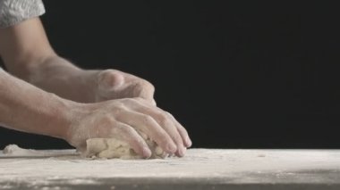 Male hands divide baking dough into three equal shares on a wooden board sprinkled with flour. Filmed on black background