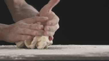 Male hands divide baking dough into three equal shares on a wooden board sprinkled with flour. Filmed on black background