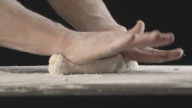 Male hands divide baking dough into three equal shares on a wooden board sprinkled with flour. Filmed on black background