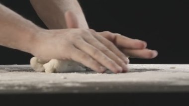 Male hands divide baking dough into three equal shares on a wooden board sprinkled with flour. Filmed on black background