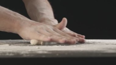 Male hands divide baking dough into three equal shares on a wooden board sprinkled with flour. Filmed on black background