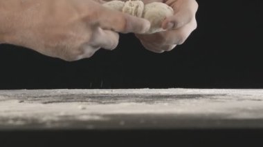 Male hands divide baking dough into three equal shares on a wooden board sprinkled with flour. Filmed on black background