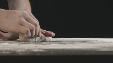 Male hands divide baking dough into three equal shares on a wooden board sprinkled with flour. Filmed on black background