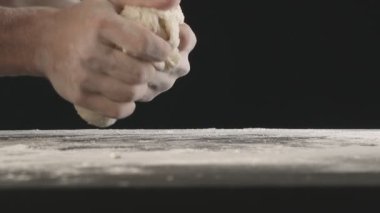 Male hands divide baking dough into three equal shares on a wooden board sprinkled with flour. Filmed on black background