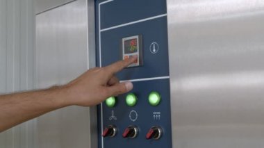 Erkek ellerinin, sanayi ekmek fırını kontrol panelinde düğme ve ekran ve alüminyum görünümlü zaman ve sıcaklık ayarlaması. Kamera elleri takip ediyor.