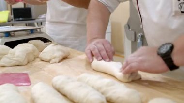 Three bakers camera filming hands work in the bakery with dough. One of them weighs pieces of dough on an electronic scale. Two others knead and shaped bread pieces after that. On the table lies a