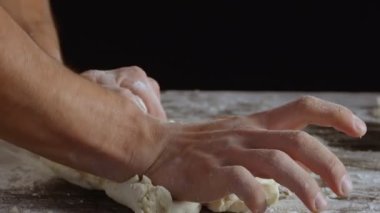 Male hands divide baking dough into three equal shares on a wooden board sprinkled with flour. Filmed on black background