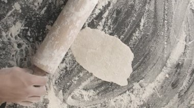 Erkek eller, un serpiştirilmiş ahşap bir tahta üzerinde merdane kullanarak hamur pişirir. Yukarıdan dikey çekim