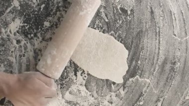 Erkek eller, un serpiştirilmiş ahşap bir tahta üzerinde merdane kullanarak hamur pişirir. Yukarıdan dikey çekim