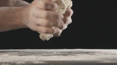 Erkek eller bir parça hamur yoğurur ve un serpiştirilmiş ahşap masanın üzerinde ikiye böler. Siyah arkaplanda çekilen