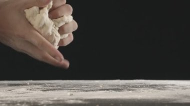 Erkek eller bir parça hamur yoğurur ve un serpiştirilmiş ahşap masanın üzerinde ikiye böler. Siyah arkaplanda çekilen