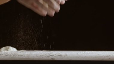Erkek eller bir parça hamuru ahşap bir masaya fırlatır ve un serperler. Siyah arkaplanda çekilen