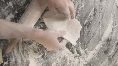 Male hands roll out baking dough using rolling pin on a wooden board sprinkled with flour than prepare area for next roll out