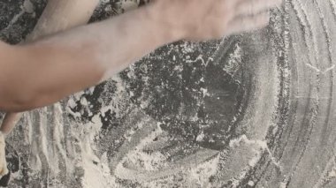 Male hands roll out baking dough using rolling pin on a wooden board sprinkled with flour than prepare area for next roll out
