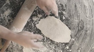 Male hands roll out baking dough using rolling pin on a wooden board sprinkled with flour than prepare area for next roll out