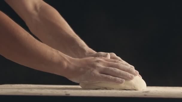 男性の手は 木製のテーブルに生地の一部をスローし 小麦粉でそれを振りかける 黒を背景に撮影 — ストック動画