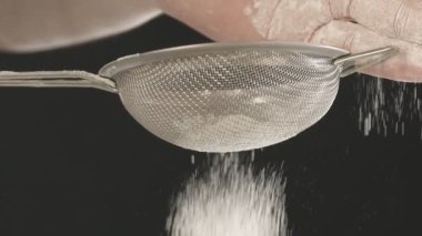 Erkek ellerinin küçük metal elek ile unu ellediği yakın plan. Siyah arkaplanda çekilen