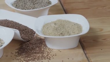 Different cereals in white dishes and scattered around on the wooden table