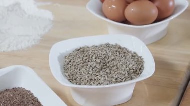 Different cereals in white dishes and scattered around on the wooden table