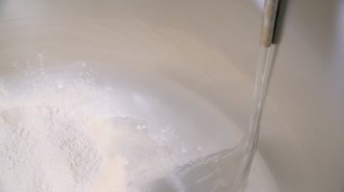 Pouring water into flour in an industrial mixer at a bread baking plant