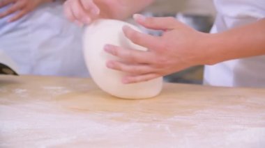 Close-up of dough kneaded by baker on a wooden board sprinkled with flour. Slow motion