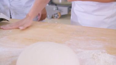 Close-up of dough kneaded by baker on a wooden board sprinkled with flour. Slow motion