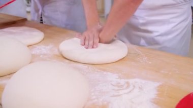 Close-up of dough kneaded by baker on a wooden board sprinkled with flour. Slow motion