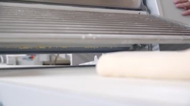 Close-up of piece of dough on the bakery dough rolling machine. Slow motion