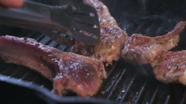 Close-up of spiced lamb ribs on the grill are turned with tongs. Slow motion