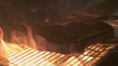 Close-up of big stake grilled on the big open fire and turned with tongs. Slow motion