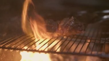Close-up of big stake grilled on the big open fire and turned with tongs. Slow motion