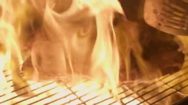 Close-up of big stake grilled on the big open fire and turned with tongs. Slow motion
