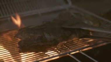 Close-up of big stake grilled on the big open fire and turned with tongs. Slow motion